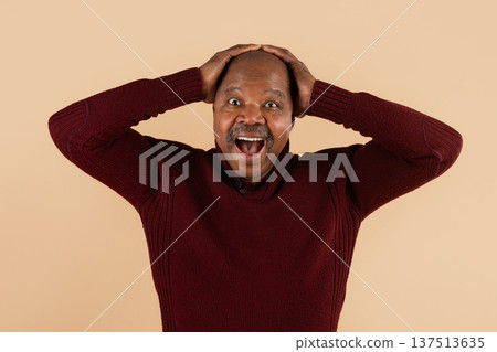 Mature black man holding head with surprised expression on beige studio background 137513635