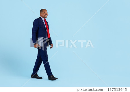 Mature african american businessman in suit walking confidently while holding laptop folder 137513645