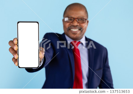 Mature african american businessman presenting blank smartphone toward camera on blue background Mature african american businessman presenting blank smartphone toward camera on blue background 137513653