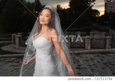 Asian bride smiling wearing wedding dress and veil in sunset lig 137513750