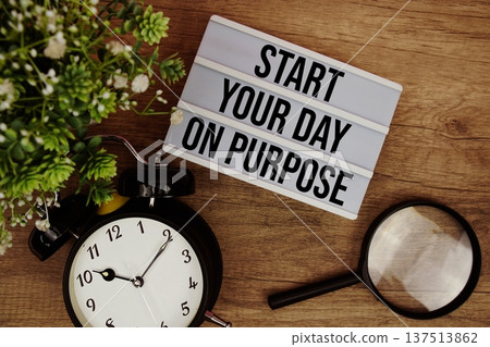 Start Your Day On Purpose text in lightbox with magnifying glass and alarm clock flat lay on wooden background Start Your Day On Purpose text in lightbox with magnifying glass and alarm clock flat lay on wooden background 137513862