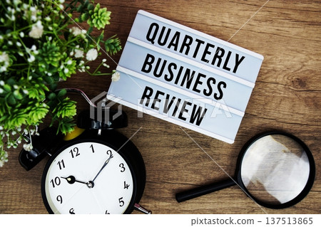 QBR Quarterly Business Review text in lightbox with magnifying glass and alarm clock flat lay on wooden background 137513865