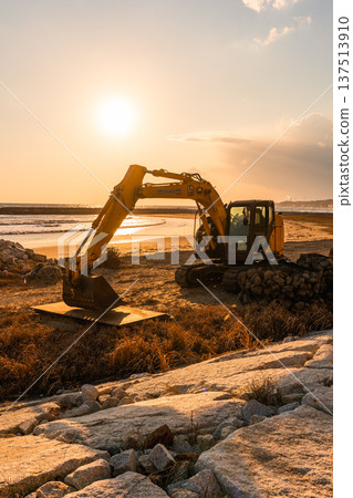 Excavator on the coast illuminated by the setting sun Excavator on the coast illuminated by the setting sun 137513910