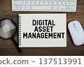 Digital Asset Management text written on notepad with keyboard, optical mouse and magnifying glass on wooden background 137513991