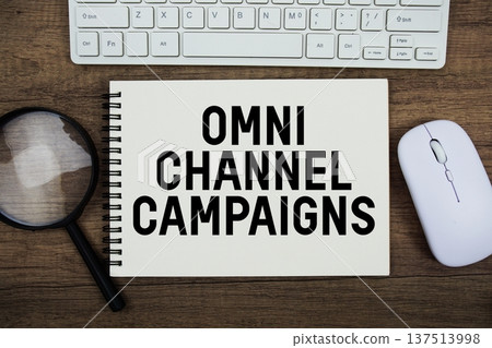 Omnichannel Campaigns text written on notepad with keyboard, optical mouse and magnifying glass on wooden background 137513998