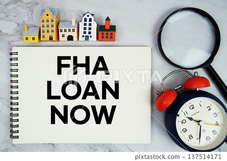 FHA Loan Now text written on notepad with house model, magnifying glass and alarm clock on marble background 137514171