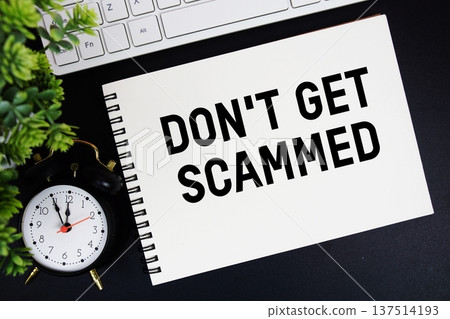 Don't Get Scammed text written on notepad with keyboard and alarm clock on black background 137514193