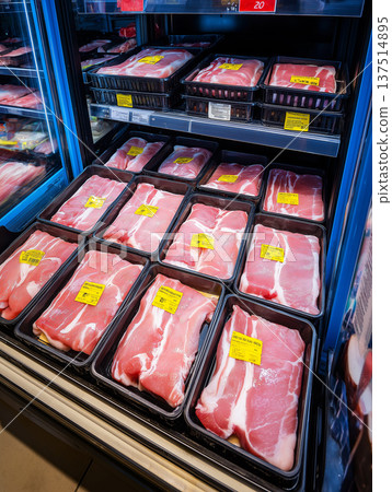 Pork chops rest in black trays at a refrigerated supermarket meat case. Bright yellow price labels mark each package. 137514895