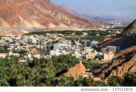Panoramic view of the traditional Fanja oasis town with palm tree groves nestled between rugged mountains in Oman. Panoramic view of the traditional Fanja oasis town with palm tree groves nestled between rugged mountains in Oman. 137515858