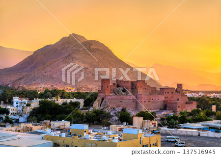 The majestic Nakhal Fort perched on a rocky outcrop against the backdrop of Hajar Mountains and a warm sunset sky in Oman. The majestic Nakhal Fort perched on a rocky outcrop against the backdrop of Hajar Mountains and a warm sunset sky in Oman. 137516945