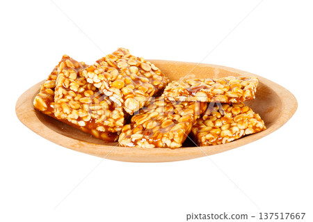Pieces of Brazilian peanut brittle, made with caramelized peanuts, arranged in a wooden bowl against a white background. A typical Brazilian sweet. Pieces of Brazilian peanut brittle, made with caramelized peanuts, arranged in a wooden bowl against a white background. A typical Brazilian sweet. 137517667