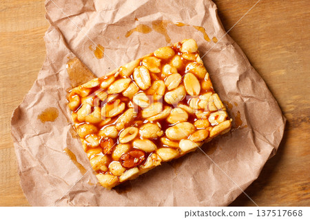 A piece of Brazilian peanut brittle made with roasted peanuts and golden caramel, on kraft paper on a rustic wooden table 137517668