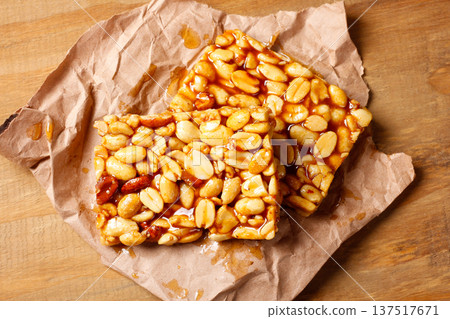 Two pieces of Brazilian peanut brittle made with roasted peanuts and golden caramel, on kraft paper on a rustic wooden table 137517671
