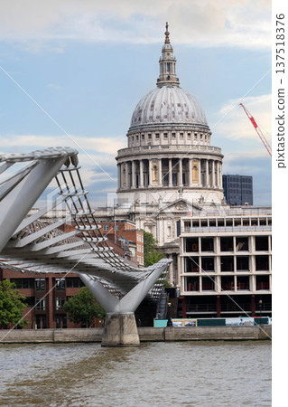 Historic architecture of St Paul Cathedral in London rises behind Millennium Bridge with pedestrians in the foreground beneath dramatic clouds in the sky. Historic architecture of St Paul Cathedral in London rises behind Millennium Bridge with pedestrians in the foreground beneath dramatic clouds in the sky. 137518376
