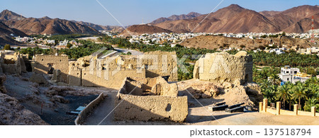 View of the ancient clay ruins and fortification walls of Fanja Fort overlooking the lush palm oasis and residential town in the Ad Dakhiliyah region, Oman View of the ancient clay ruins and fortification walls of Fanja Fort overlooking the lush palm oasis and residential town in the Ad Dakhiliyah region, Oman 137518794