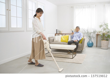 A smiling woman and a man in their 60s vacuuming while having a conversation 137519812