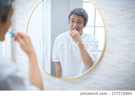 一位六十多歲的男子一邊刷牙一邊照鏡子 一位六十多歲的男子一邊刷牙一邊照鏡子 137519960