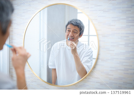 一位六十多歲的男子一邊刷牙一邊照鏡子 一位六十多歲的男子一邊刷牙一邊照鏡子 137519961