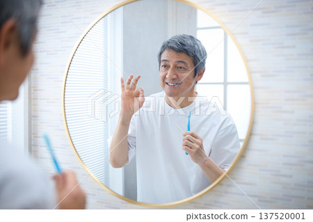 一位六十多歲的微笑的男子拿著牙刷,正在照鏡子。 一位六十多歲的微笑的男子拿著牙刷,正在照鏡子。 137520001