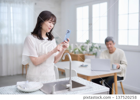 A woman in her 60s looking at her smartphone in the kitchen 137520258