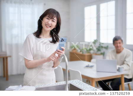 一位六十多歲的婦女在廚房裡看著她的智慧型手機。 137520259