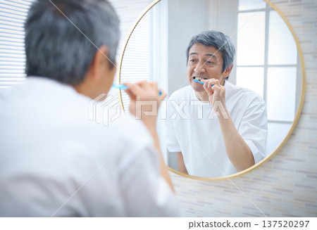 一位 60 多歲的男子一邊刷牙一邊照鏡子 137520297