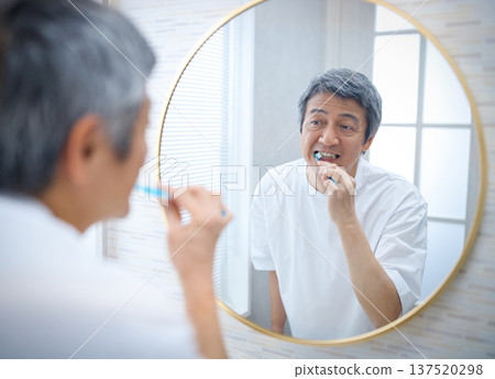 A man in his 60s brushing his teeth while looking in the mirror A man in his 60s brushing his teeth while looking in the mirror 137520298