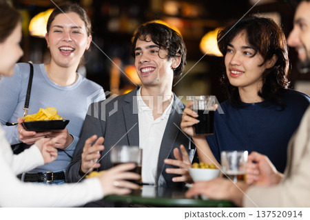 Group of positive young friends talking cheerfully and drinking beer at table in bar 137520914