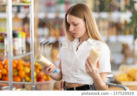 Choose food in supermarket - woman chooses mayonnaise to buy in the grocery department section of store 137520929