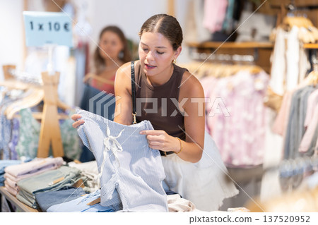 Girl customer chooses trousers in store, and buyer carefully examines product. Girl customer chooses trousers in store, and buyer carefully examines product. 137520952