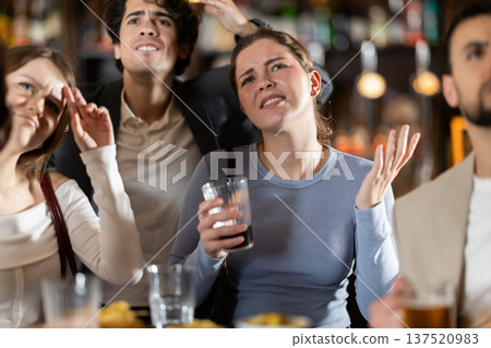 Emotional sad group of young sports fans man and woman worrying about defeat sports team, watching match on TV during rest in beer bar 137520983