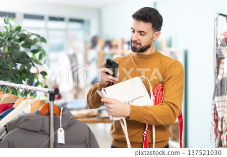 Young man scans qr code of women's handbag in store 137521030
