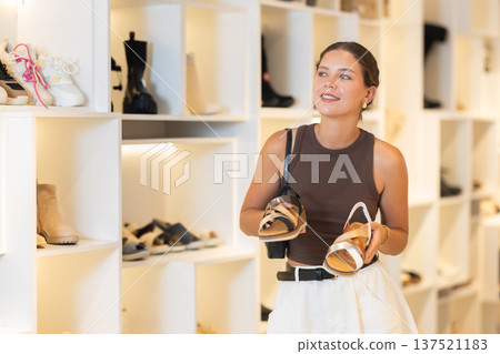 Girl customer chooses sandals in store, and buyer carefully examines product. Girl customer chooses sandals in store, and buyer carefully examines product. 137521183