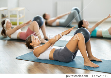 Young woman with athletes group hold fitball in lap knee , raise and lower torso 137521319