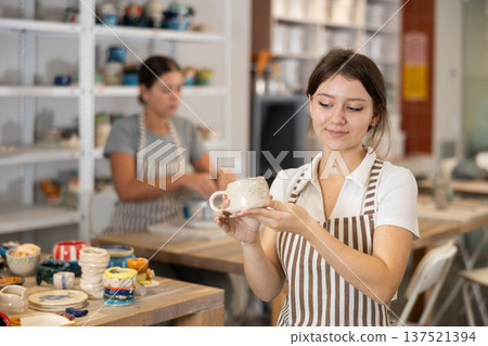 Girl stands in pottery workshop and shows created work, finished decorative vase - jug. Girl stands in pottery workshop and shows created work, finished decorative vase - jug. 137521394