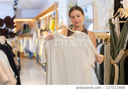 Girl customer chooses blouse in store, and buyer carefully examines product. 137521400