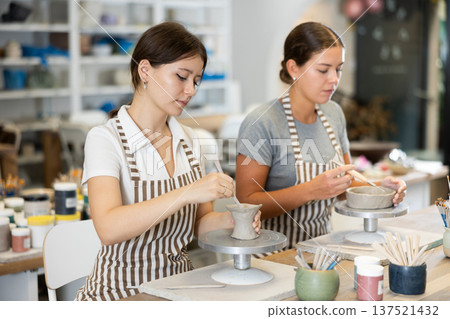 Two young women pottery workshop workers sculpt from raw clay 137521432
