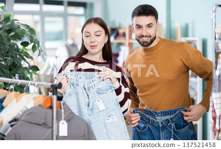 Woman selects jeans in clothing store. Man helps her Woman selects jeans in clothing store. Man helps her 137521458