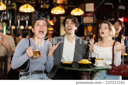 Group of emotional football fans watching match of favorite team at table in sports bar, and screaming chants together Group of emotional football fans watching match of favorite team at table in sports bar, and screaming chants together 137521591