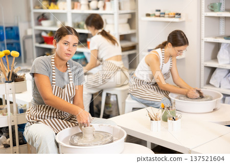 Three young women sits near potter wheel and makes clay crafts 137521604