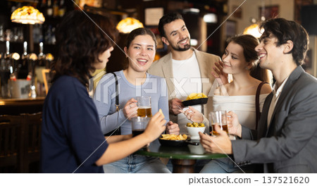 Young friends meeting at table in bar, discussion and drinking beer 137521620