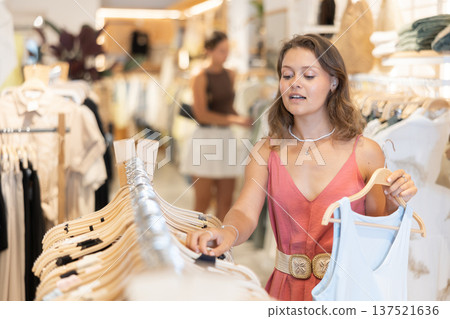 Positive joyful young woman looking for fashionable clothes in clothing boutique Positive joyful young woman looking for fashionable clothes in clothing boutique 137521636