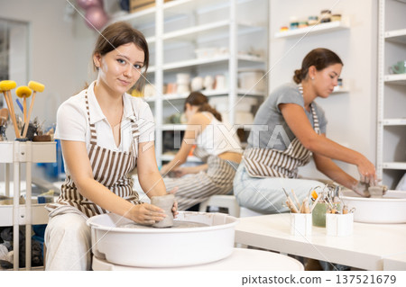 Three young women sits near potter wheel and makes clay crafts Three young women sits near potter wheel and makes clay crafts 137521679