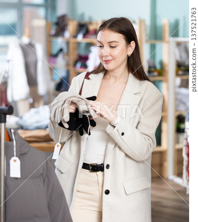 Focused young female client choosing warm gloves for winter season in clothing store Focused young female client choosing warm gloves for winter season in clothing store 137521763
