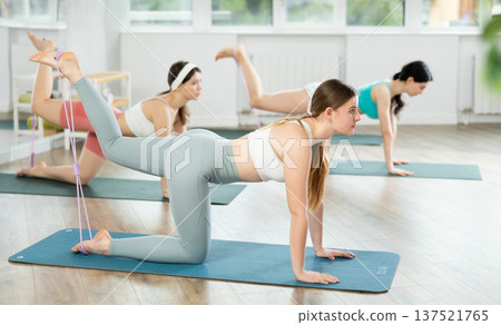 Girl leads class women, standing on all fours, performing exercises with wide elastic skip rope Girl leads class women, standing on all fours, performing exercises with wide elastic skip rope 137521765