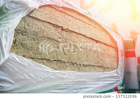 Stack of mineral wool thermal insulation material wrapped in protective plastic film at a construction site or warehouse. 137522036