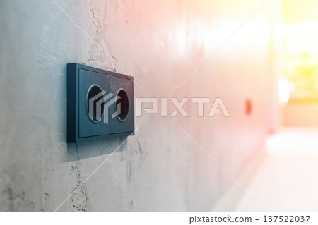 Close-up of modern black power outlets installed on a grey concrete wall in a minimalist loft interior. Electrical sockets in a workspace. Close-up of modern black power outlets installed on a grey concrete wall in a minimalist loft interior. Electrical sockets in a workspace. 137522037