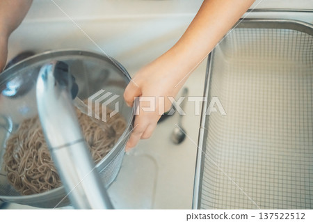 一位家庭主婦從濾鍋裡取出蕎麥麵,用冷水沖洗。 一位家庭主婦從濾鍋裡取出蕎麥麵,用冷水沖洗。 137522512