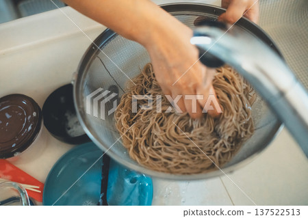 A housewife takes boiled soba noodles out of a colander and washes them with cold water A housewife takes boiled soba noodles out of a colander and washes them with cold water 137522513