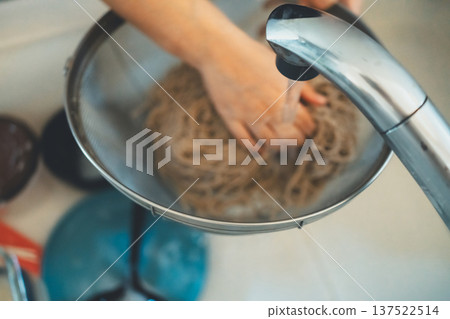 一位家庭主婦從濾鍋裡取出蕎麥麵，用冷水沖洗。 137522514